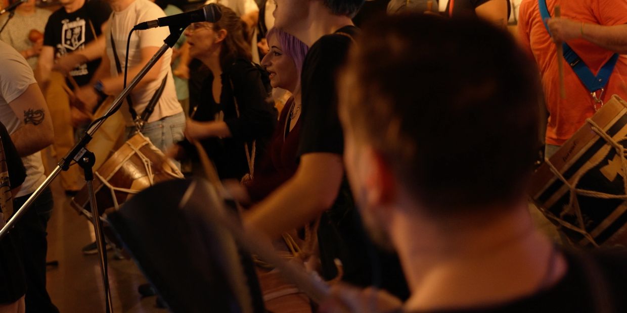 People playing drums and singing at a lively gathering.