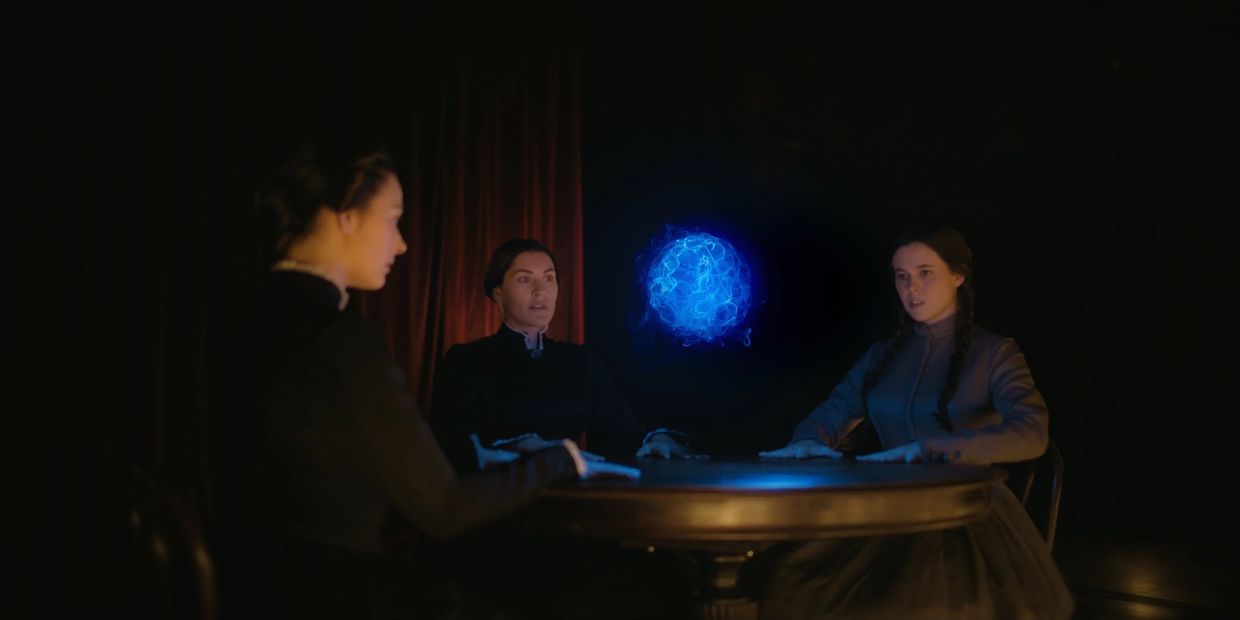 Three women around a table with a glowing blue orb.