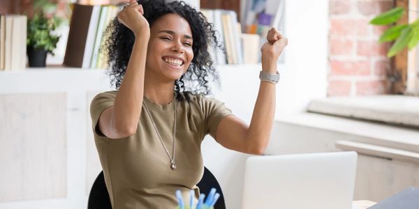 Woman celebrating success while sitting at her desk with a laptop.