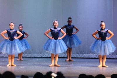 Young ballerinas in blue tutus pose on stage during a recital.