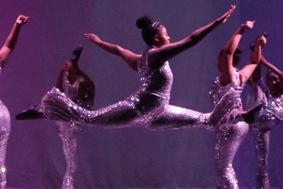 Dancers in silver costumes performing a leap on stage.