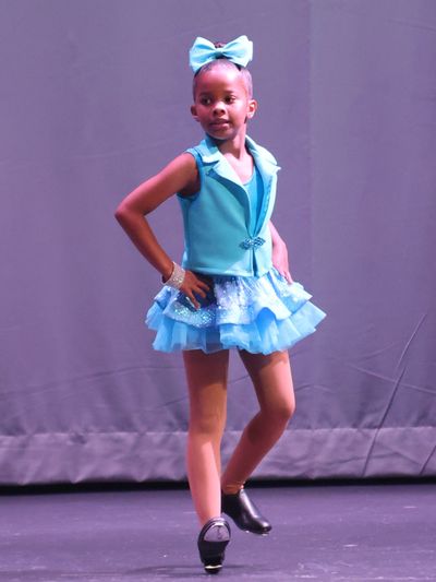 Young girl in blue dance costume poses on stage.