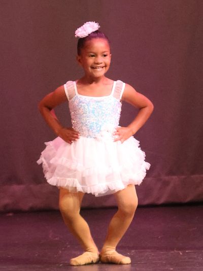 Young girl smiling in a white ballet costume on stage.