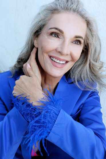 Smiling mature woman in a vibrant blue feathered jacket.