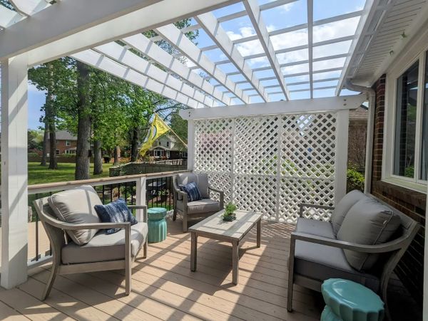 Sofa & chairs under a white pergola, lattice wall, PVC decking with vinyl railings. 