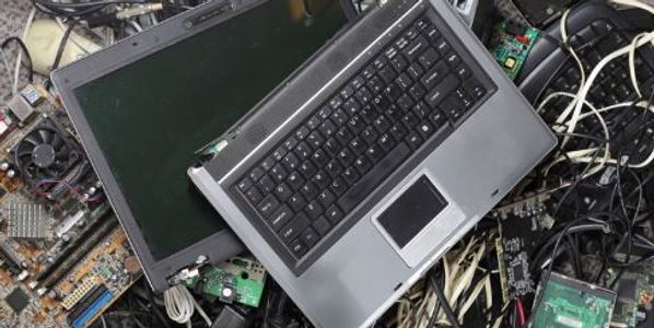 Dismantled laptop atop a pile of discarded cables, mother boards, and other electronic waste.