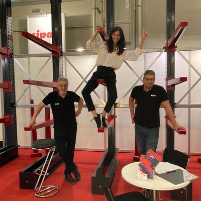 Three people posing on and around red and black metal racks at an indoor event.
