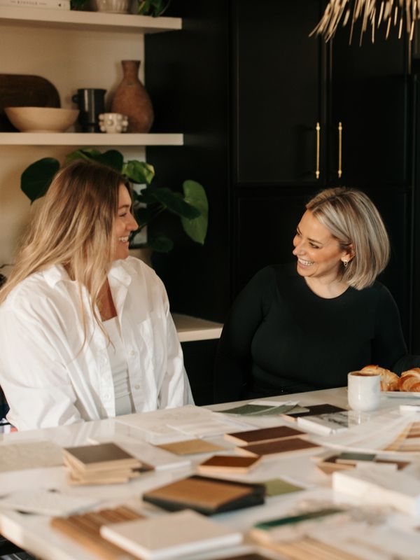 Two women smiling and discussing over design samples at a table.