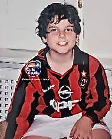 A young boy in a red and black striped soccer jersey.