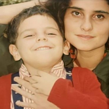 A woman lovingly hugs a smiling young boy.