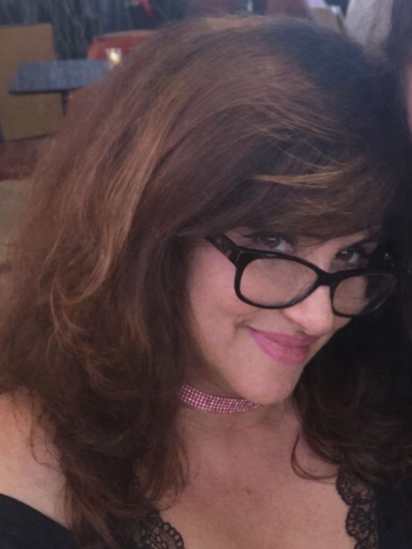 Woman with glasses smiling, wearing a pink choker and black lace top.
