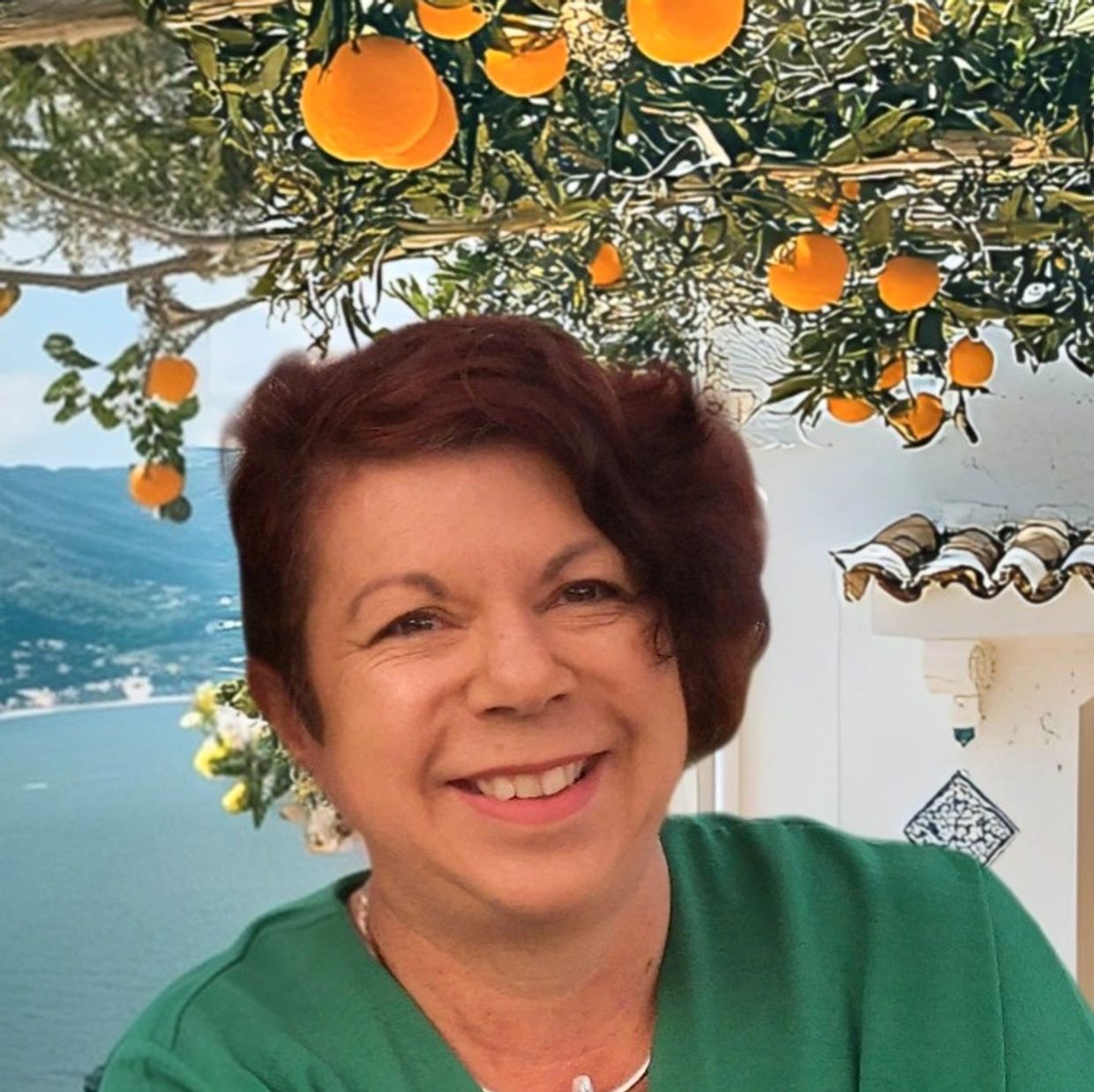 Smiling woman in green with oranges hanging above and a sea view.