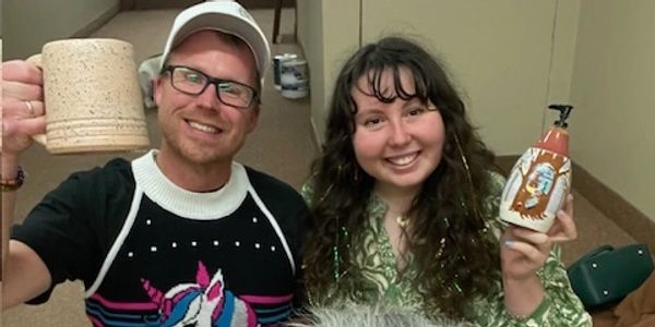 Three people smiling indoors, one holding a mug and another holding a decorative bottle.
