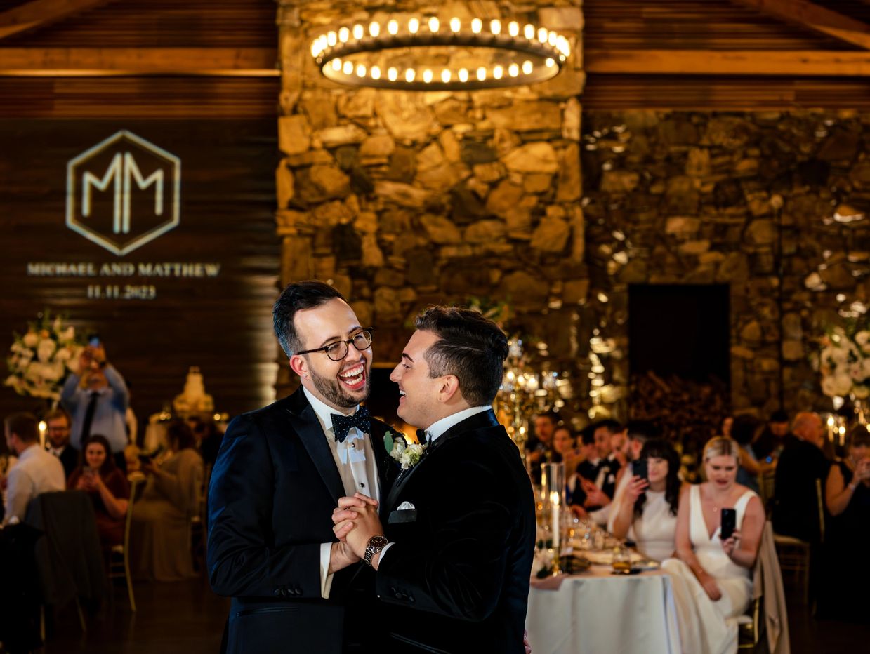 Two grooms dancing at their asheville wedding at the Grove Park with a custom monogram on the wall