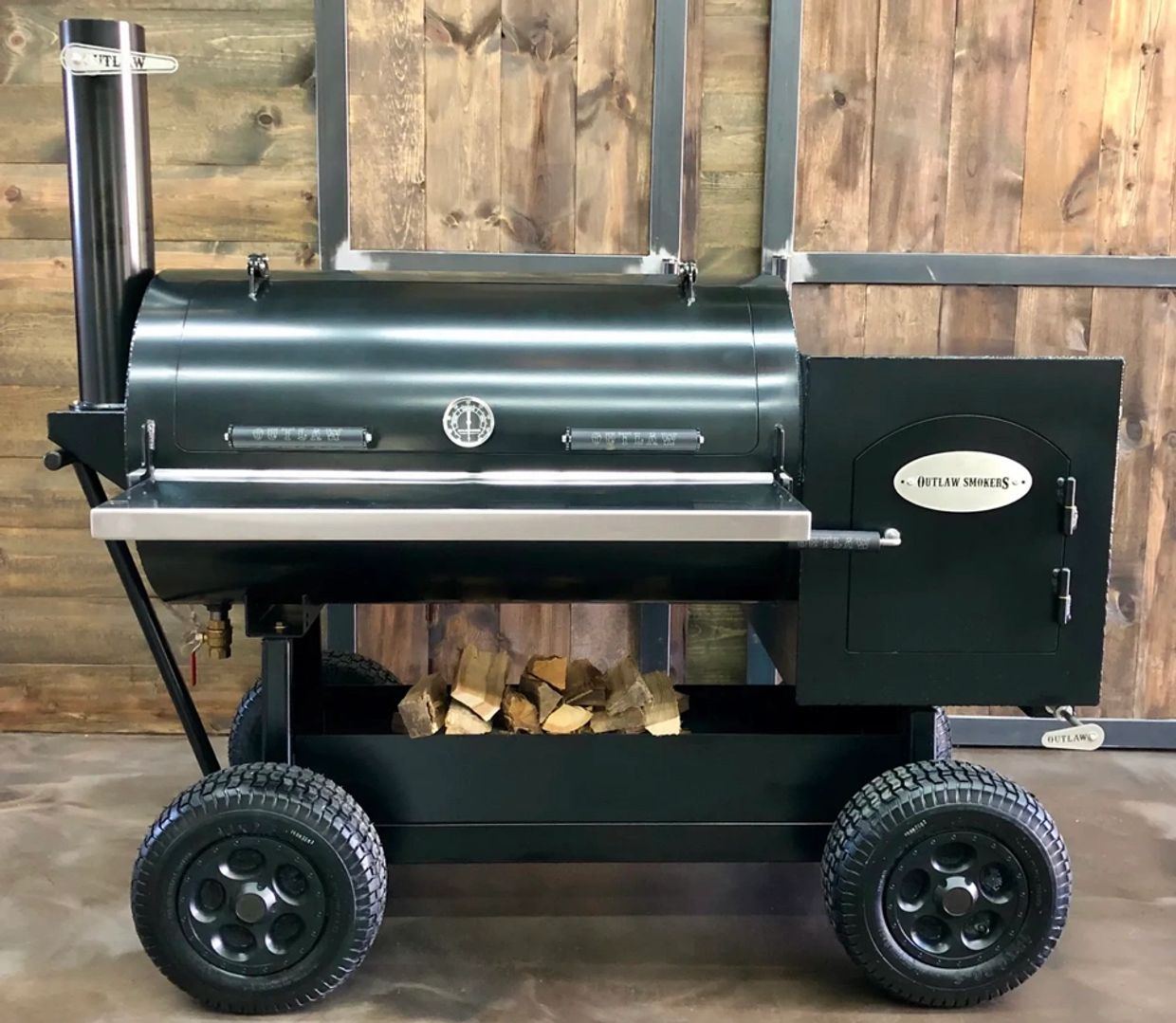 Large black outdoor smoker grill on wheels with wood storage underneath.