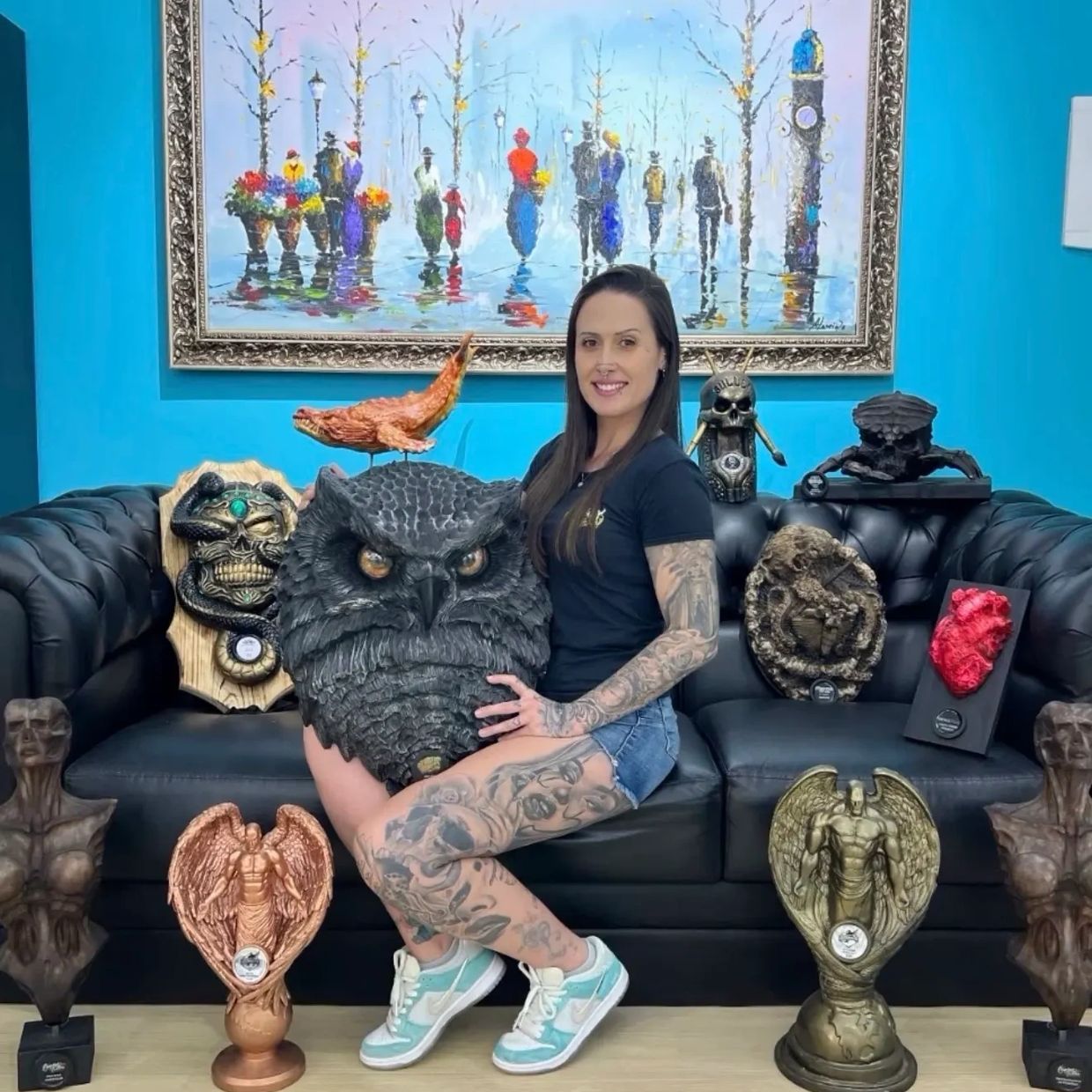 Tattooed woman posing with detailed sculptures on a black couch.