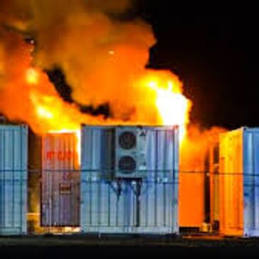 Large fire engulfing a structure behind three industrial air conditioning units at night.