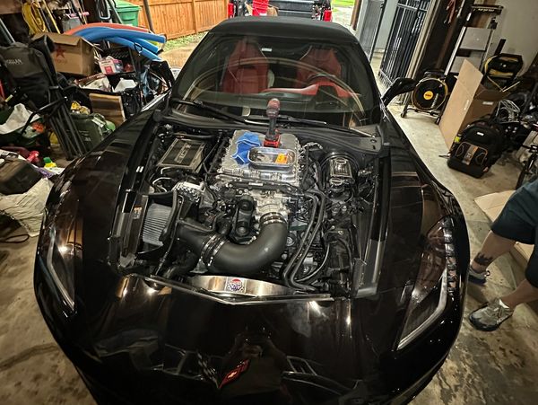 Black sports car with exposed engine in a cluttered garage.