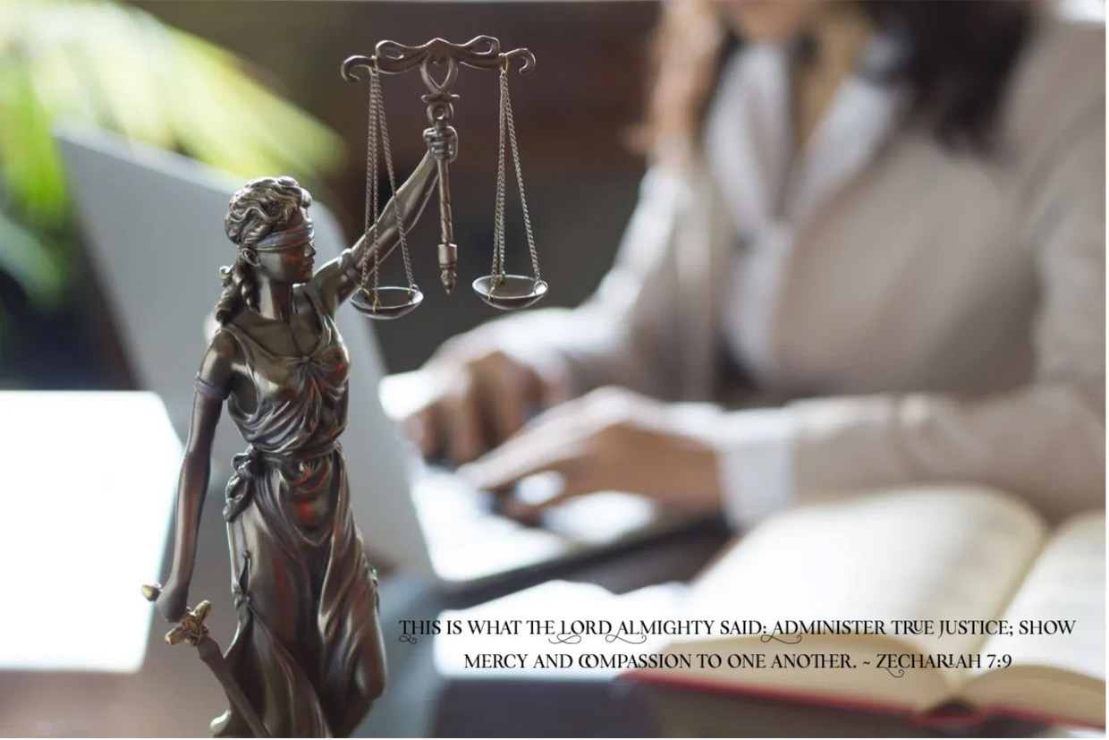 a lady sitting at a desk with a laptop and a statue of lady justice