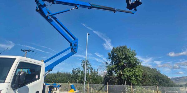 A white truck with an extended blue hydraulic lift arm under a clear blue sky.