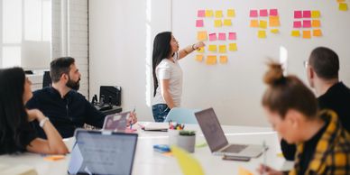 Alt="woman pointing to strategy board in an office with team"