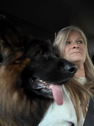 Woman with long hair sitting next to a large dog with tongue out.
