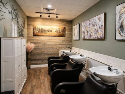Modern salon washing area with black chairs and artistic wall decor.