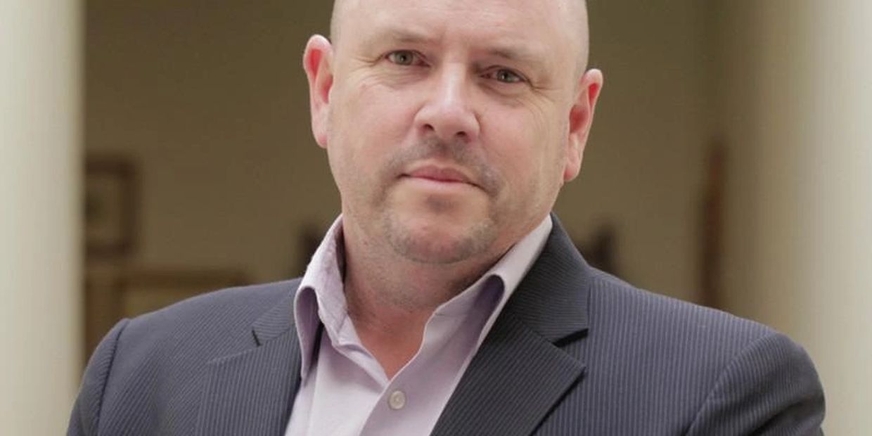 Confident bald man in a suit posing with a neutral expression.