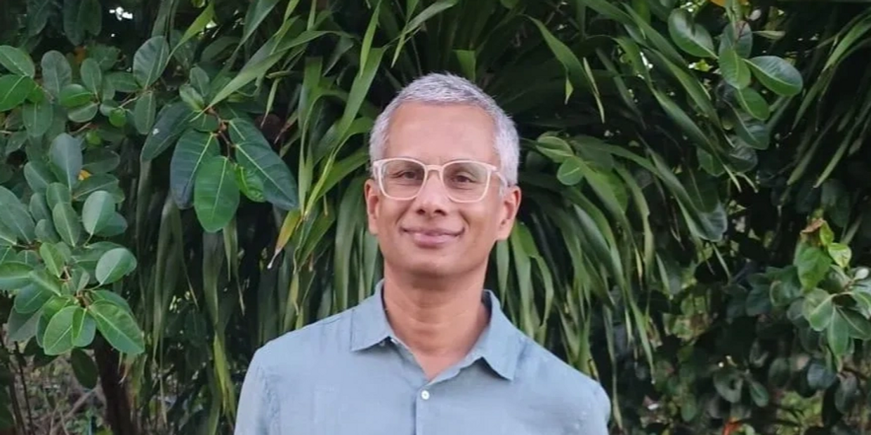 Man with glasses and gray hair stands outdoors with hands in pockets.