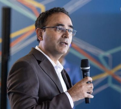 Man in glasses speaking into a microphone at an event.