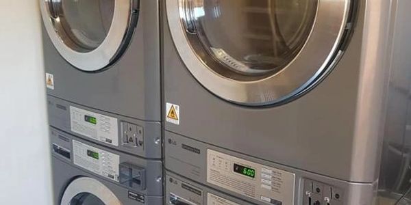 Two stacked sets of industrial washers and dryers.
