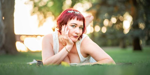 Woman with red hair lying on grass outdoors looking thoughtfully.