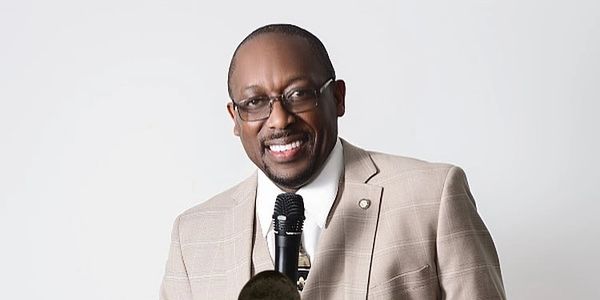 Man in beige suit speaking at a press conference.