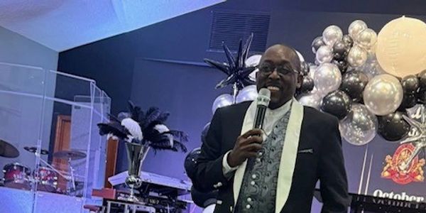 Man in tuxedo speaking with microphone at an event.