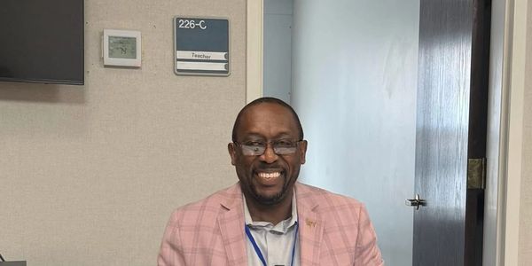 A man named Lee Wright smiles sitting behind a table in a classroom.