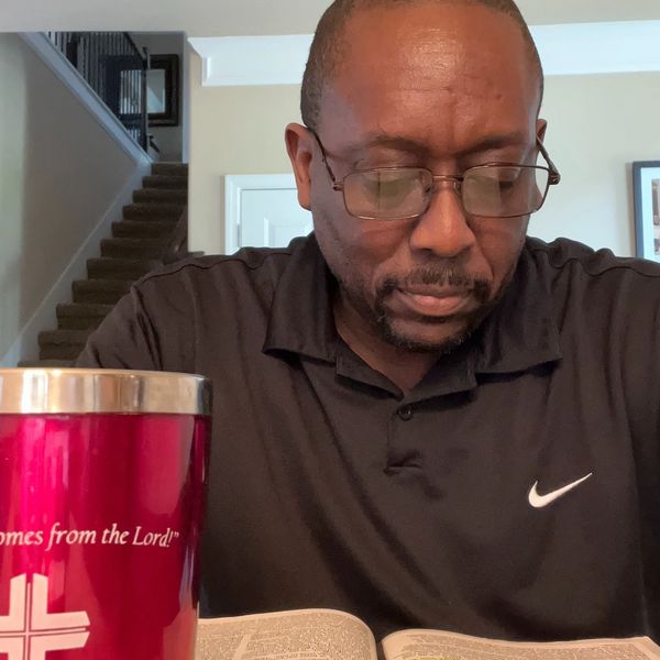 Man reading a book with a red cup nearby.