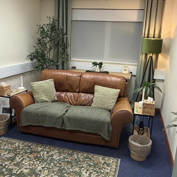 Cozy brown leather sofa with green cushions and throw in a calm room.