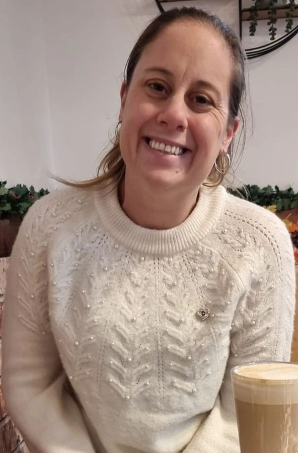 Smiling woman in a cozy white sweater sitting with a latte.