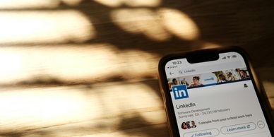 Smartphone displaying LinkedIn page under warm light shadows.