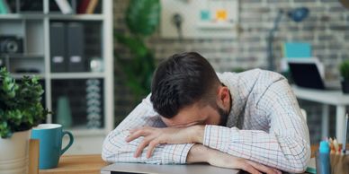 Tired man resting head on folded arms at desk.