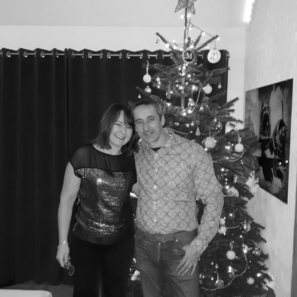 A smiling couple posing near a decorated Christmas tree indoors.