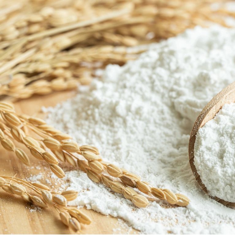Wheat stalks lying next to a pile of white flour on a wooden surface.