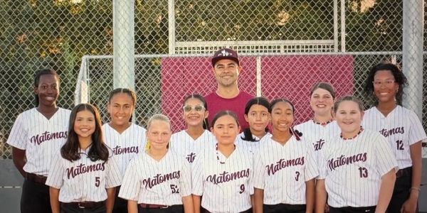 Youth softball team posing together in matching uniforms on the field.