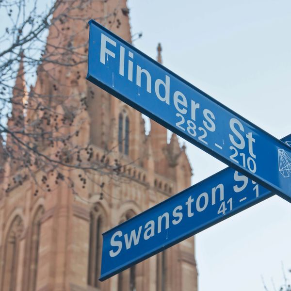 Street signs for Flinders St and Swanston St with a historic building backdrop.