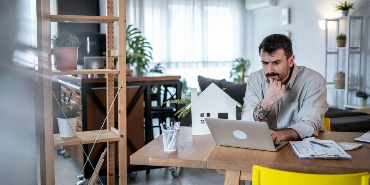 Man working on laptop with house model on table.