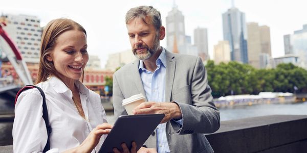 Two professionals using a tablet outdoors in a city setting.