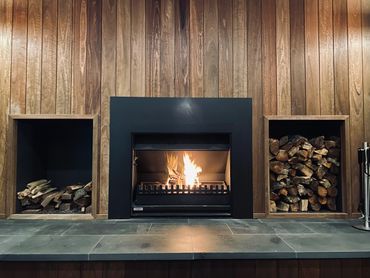 Modern indoor fireplace with wood storage and wooden panel wall.
