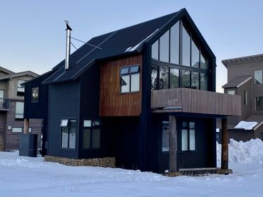 Modern black house with large windows and snow surrounding it.