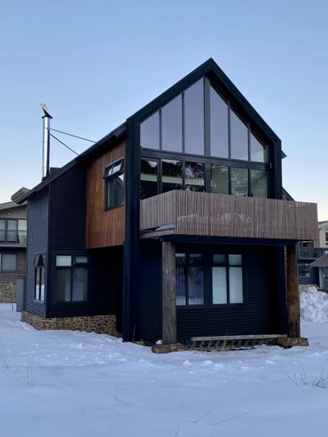 Modern two-story house with large windows and wood accents in a snowy setting.