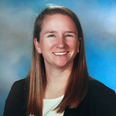 Smiling woman with long hair in professional attire against a blue backdrop.